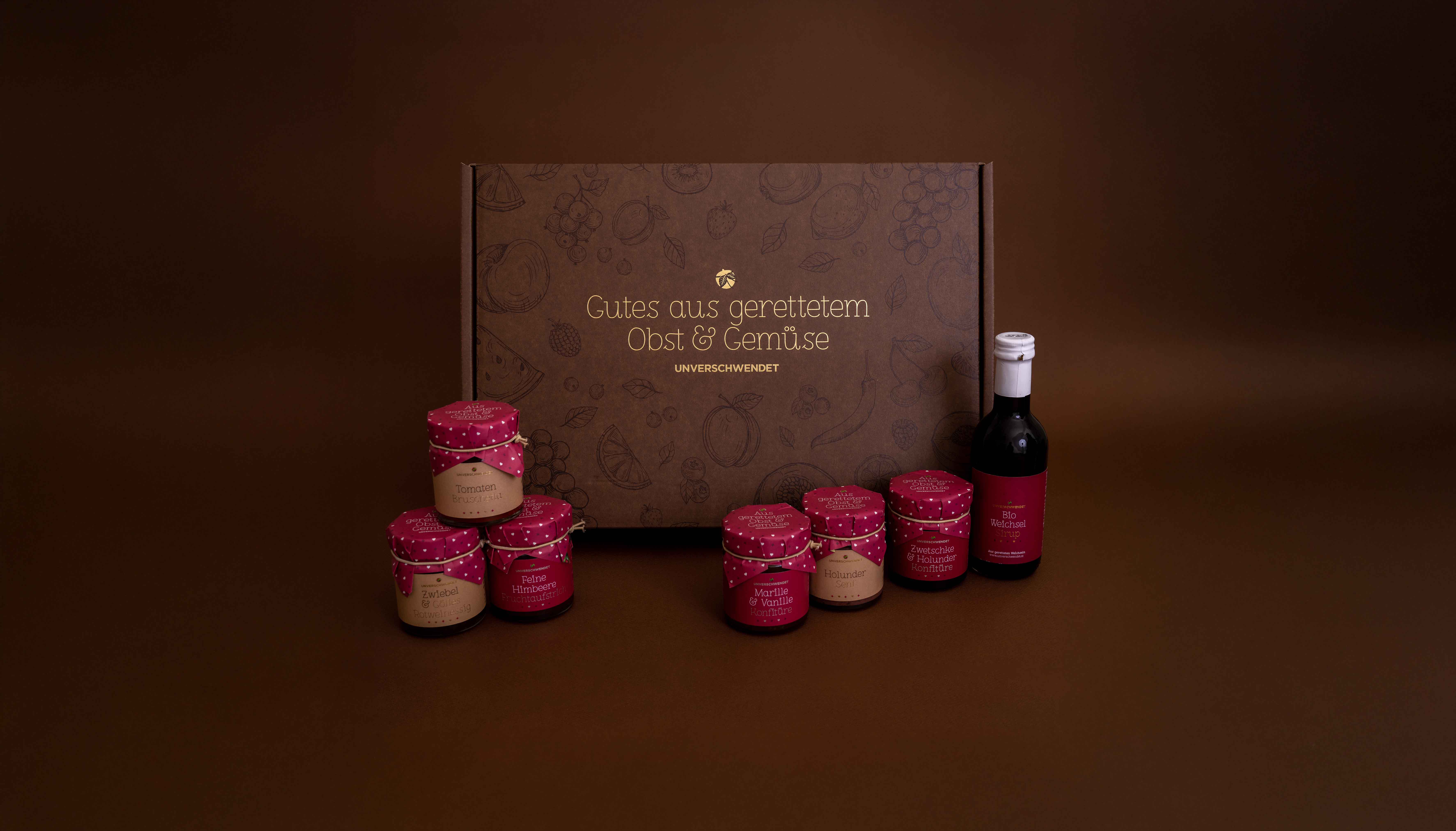 Unverschwendet-Aufstrich Gläser und Sirup mit geschenkbox im Hintergrund Unverschwendet-Aufstrich Gläser und Sirup mit geschenkbox im Hintergrund