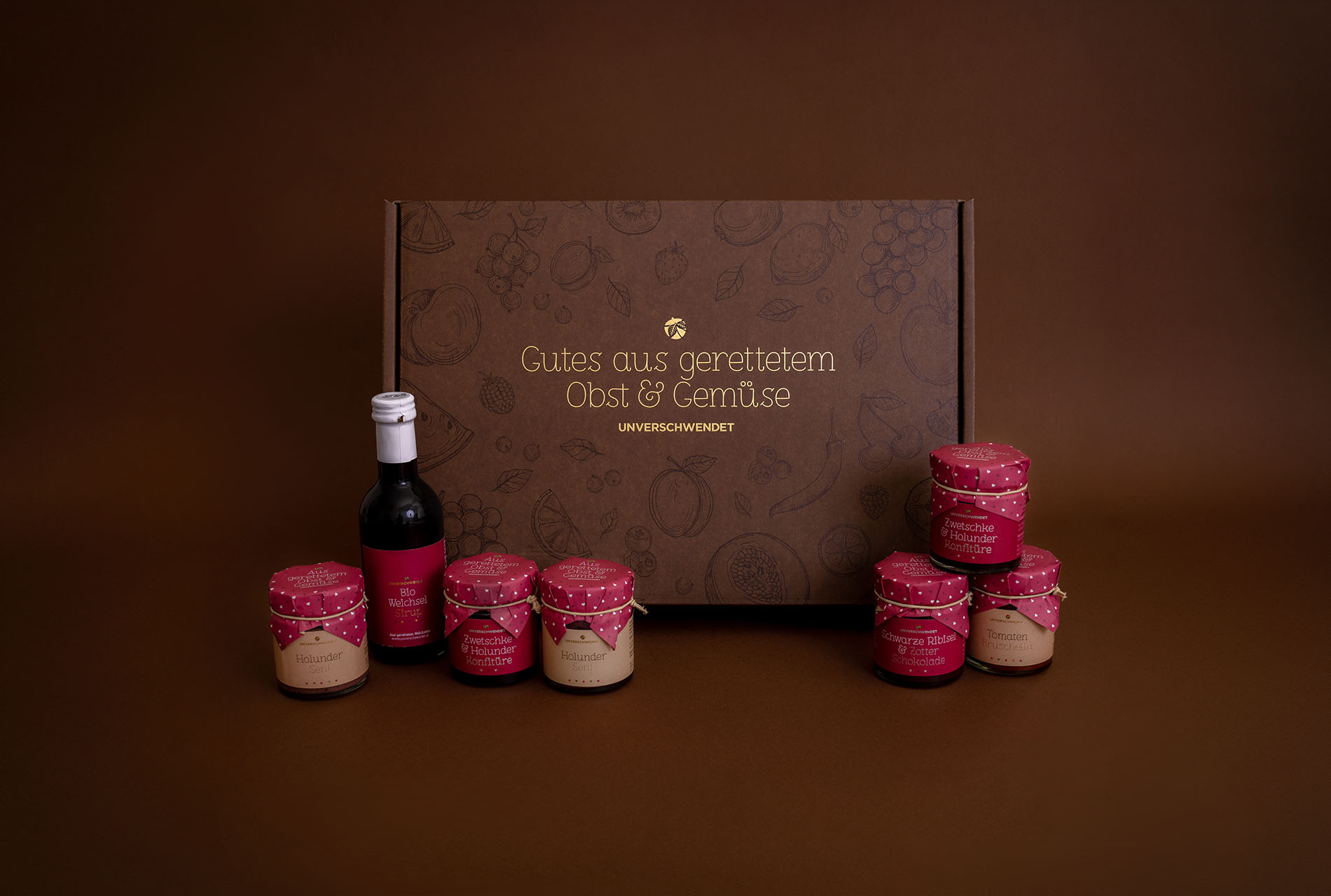 Geschenkbox-Set mit Aufstrich-Gläschen und Sirup (vor braunem Hintergrund) Geschenkbox-Set mit Aufstrich-Gläschen und Sirup