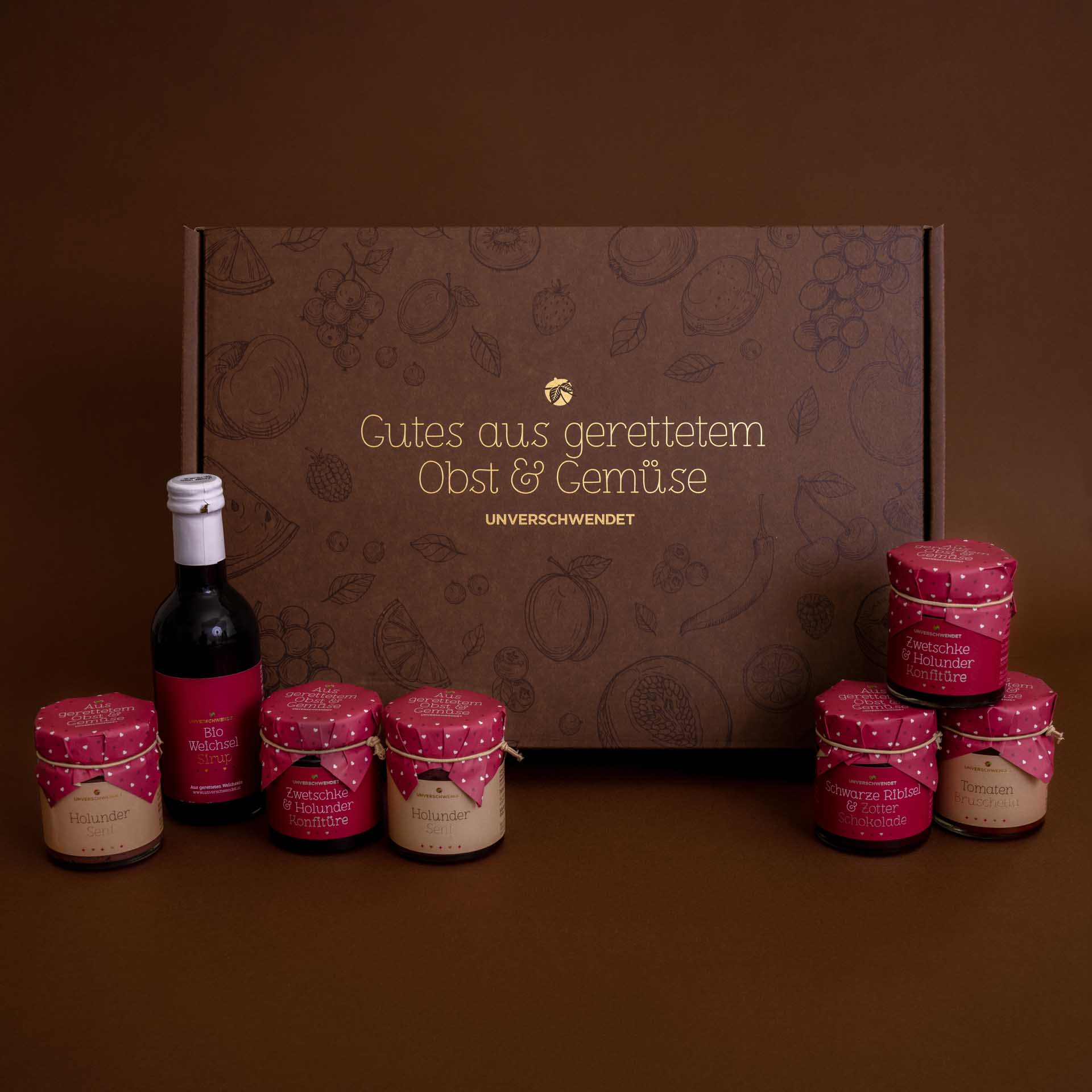 Unverschwendet-Aufstrich in Gläsern und Sirup mit Geschenkkarton im Hintergrund Unverschwendet-Aufstrich in Gläsern und Sirup mit Geschenkkarton im Hintergrund